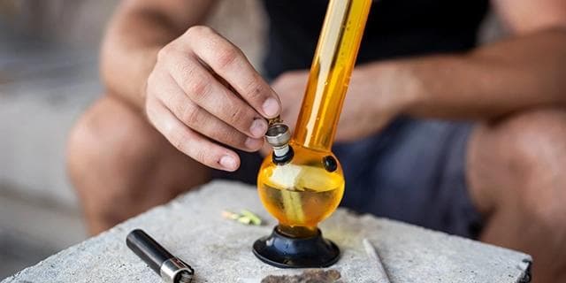 A person using a bong for consuming cannabis flower, illustrating the prolonged high associated with this method.