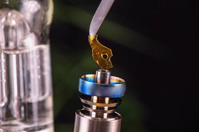 A person holding a dab tool with a piece of cannabis concentrate, preparing for the dabbing process.