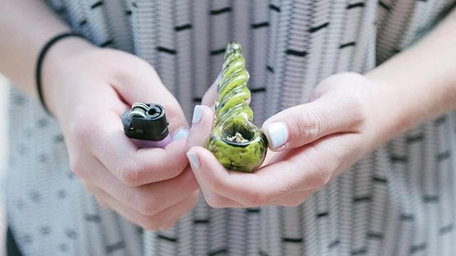 Close-up of hands meticulously packing cannabis into a green bowl, demonstrating proper technique.