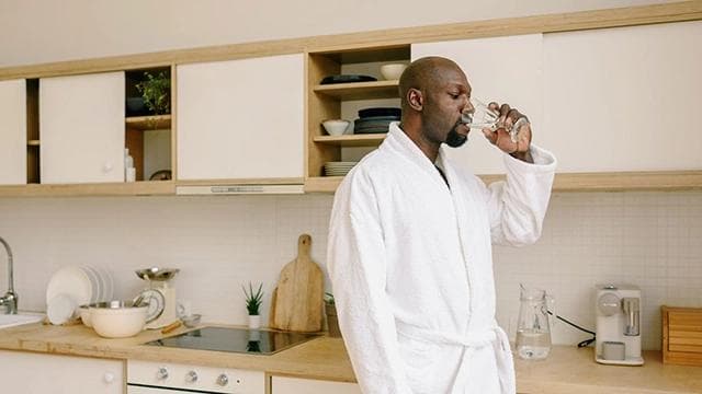 A man in a robe in his kitchen hydrates wi