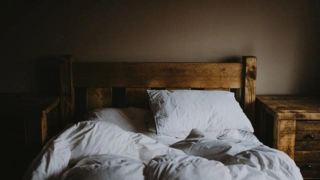 An unmade bed in a dimly lit room, symbolizing the peaceful and deep sleep that can be facilitated by the right Indica cannabis strain.