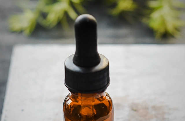 A brown glass bottle with a black dropper full of cannabis tincture on a wooden surface