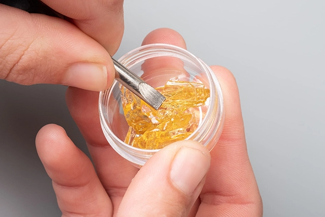 A person holding a dab tool with a piece of cannabis concentrate, preparing for the dabbing process.