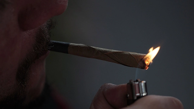 A close-up of a hand holding a lighter to the end of a pre-roll joint.