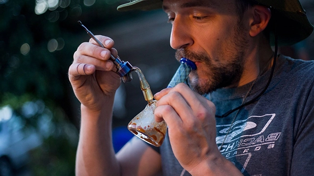 A close-up of a person inhaling from a dab rig, a method of consuming concentrated cannabis wax for a potent effect.