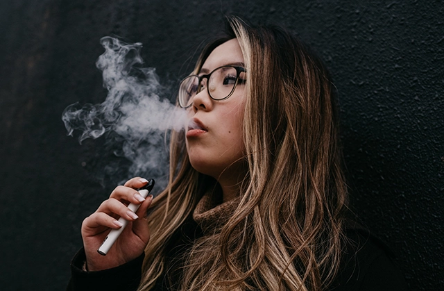 A person inhaling from a vape pen, with vapor visible around their mouth and nose, showcasing use of the device
