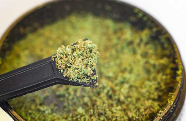 Close up of a tool being used to extract collected kief from the bottom of a grinder